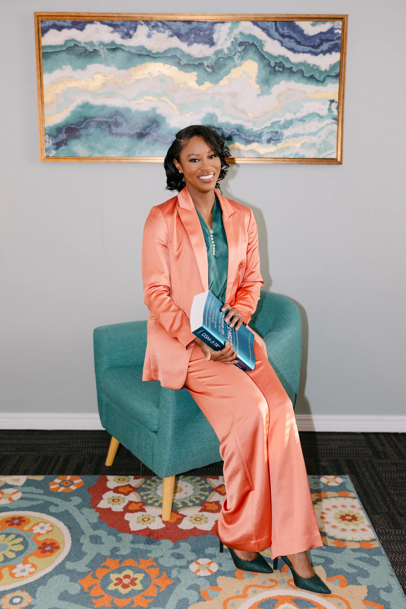 Wansley Harrison seated in a coral suit holding a social work reference book